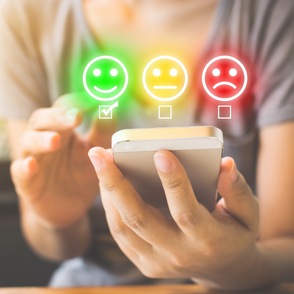 hand holding a phone with colored emojis, happy, sad, and neutral faces